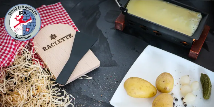 Racletteofen mit Käseschaber. Auf weissem Teller geschwellte Kartoffeln, weisse Essigzwiebeln und Cornichon.