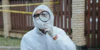 Un enquêteur de la police scientifique, vêtu d'une tenue de protection, examine une scène de crime à l'aide d'une loupe