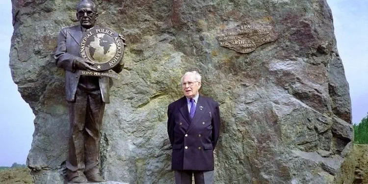 Arthur Troop se tient devant un rocher, à côté de sa statue